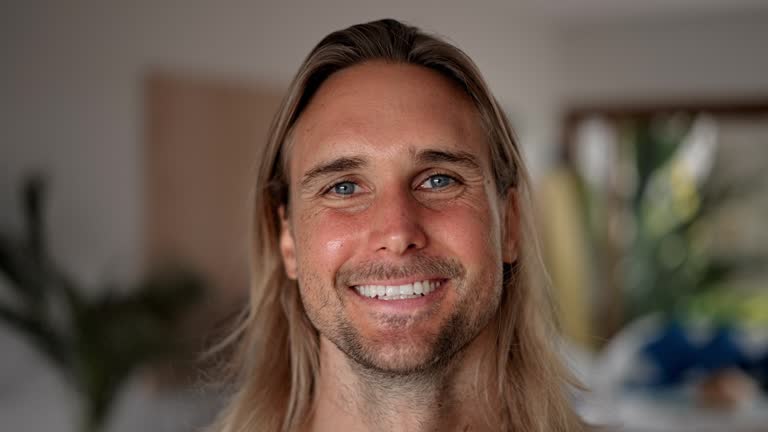 Male guy look camera. Smile face portrait. Blue eyes close up. Long hair surfer.