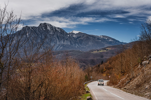 Beautiful mountain landscape, white car on an empty road in the mountains overlooking the snowy peaks