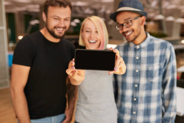 Soft focus of happy woman taking selfie with diverse boyfriends via smartphone with black screen during friends meeting in weekend