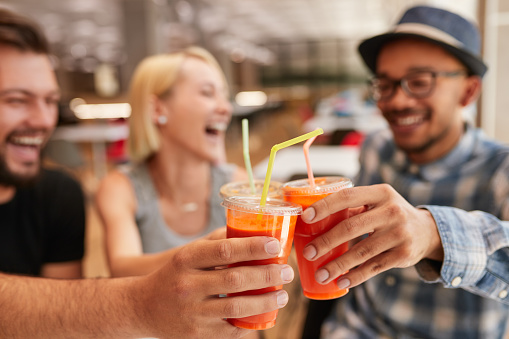 Soft focus of multiracial men and woman in casual clothes laughing and clinking cups of fresh juice on weekend day in restaurant