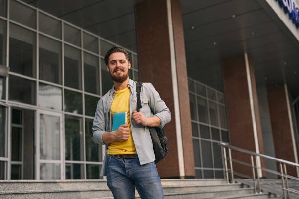 istock Content bearded guy with backpack standing on stairs of college building 1475819285