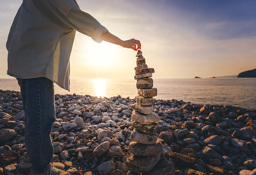 Woman building a cairn on the seashore at sunset. Zen relaxation and meditation concept