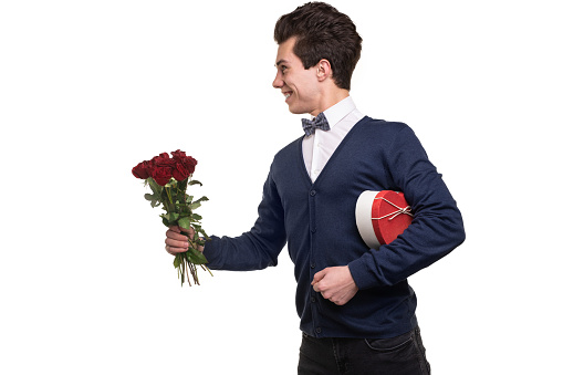 Happy young man with heart shaped gift box looking away with smile and giving red roses during date against white background