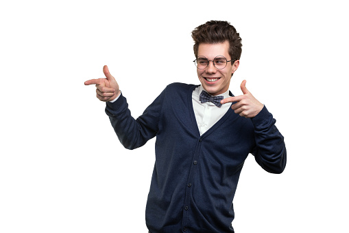 Young male student in smart casual clothes and glasses smiling and pointing away against white background