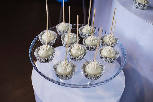 Cake pops with white chocolate and decor on glass cakestand, meringues and cupcakes. Candy bar. Sweets buffet at restaurant for birthdar, wedding, anniversary party.