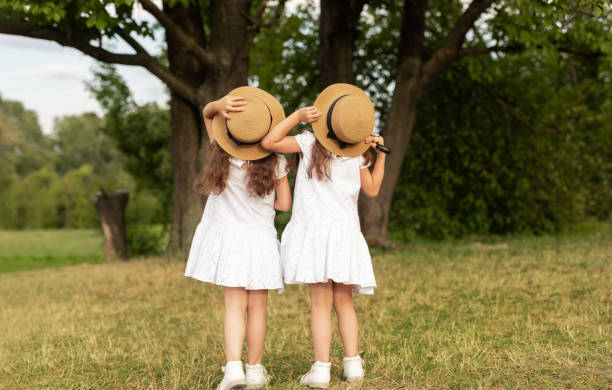 Two children are interacting outdoors during a beautiful autumn sunset, with the brother carefully placing a hat on his sister's head, showing affection and sibling bond