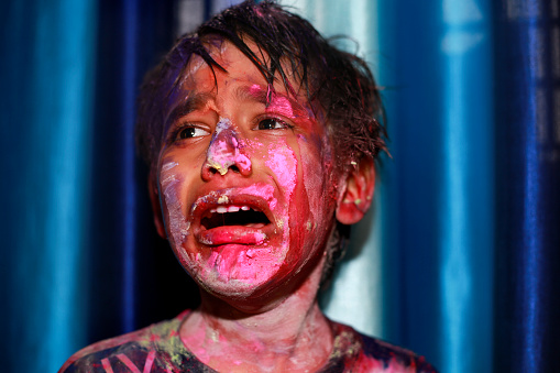 Young boy of Indian ethnicity playing with Holi colored powder and crying after someone throwing Holi colors in his mouth and eyes.