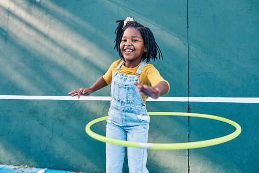 Happy, playing and portrait of a child with a hula hoop for fitness, practice and hobby. Smile, carefree and an African girl with a toy for happiness, playtime and break on a school playground