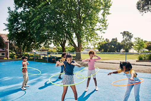 Hula hoop, children and kids playing outdoors in a park together having fun in happiness and joy for fitness. Exercise, bonding and young people practice and learning on school grounds on a break
