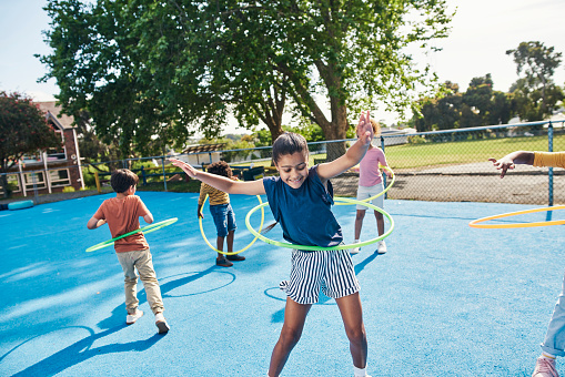 Children, hula hoop and friends playing outdoor together during break or recess on a school playground. Kids, games or fun with girl and boy students bonding while having fun outside during summer