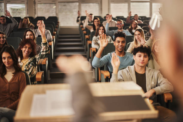 istock Happy college students raising their hands on a class at lecture hall. 1475830179