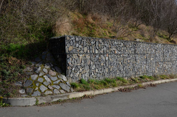 construction of a gabion retaining wall, as part of the house fencing. workers put geotextiles and on it wire baskets which consists of granite stones. demanding manual work construction of a gabion retaining wall, as part of the house fencing. workers put geotextiles and on it wire baskets which consists of granite stones. demanding manual work, excavator, geotextile, stabilization, workspace, erosion control stock pictures, royalty-free photos & images