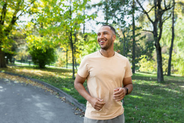 cheerful and successful hispanic man jogging in the park, man running on a sunny day, smiling and happy having an outdoor activity - 競走賽 個照片及圖片檔