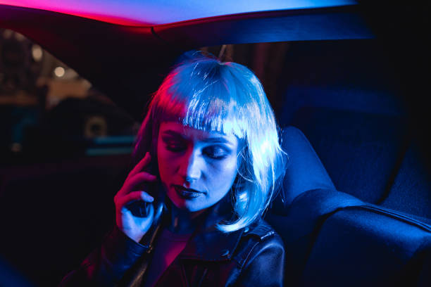 Female portrait of woman who using mobile phone indoors the car. Film Noir Style and cyberpunk concept photography, cinematic photo with neon light. Person with blue hairstyle, people and technology in vehicle. retrato femenino de una mujer que usa el teléfono móvil en el interior del automóvil. film noir style y fotografía conceptual cyberpunk, foto cinematográfica con luz de neón. persona con peinado azul, personas y tecnología en el vehículo.