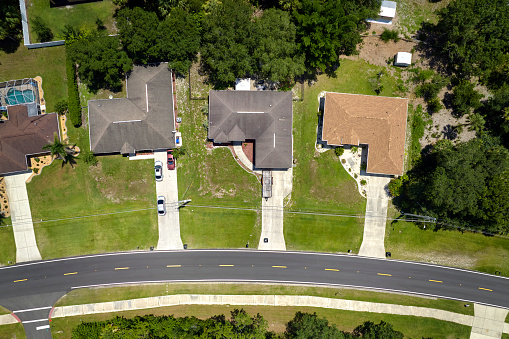 Aerial view of street traffic with driving cars in small town. American suburban landscape with private homes between green palm trees in Florida quiet residential area.