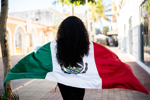 Woman walking while holding a mexican flag in the street
