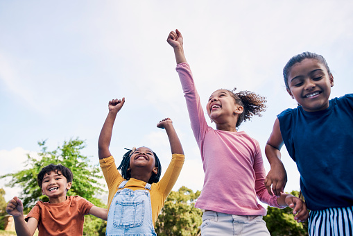 Children, freedom and energy with friends cheering together outdoor while having fun during the day. Kids, energy or diversity with a girl and boy group playing or bonding outside in summer