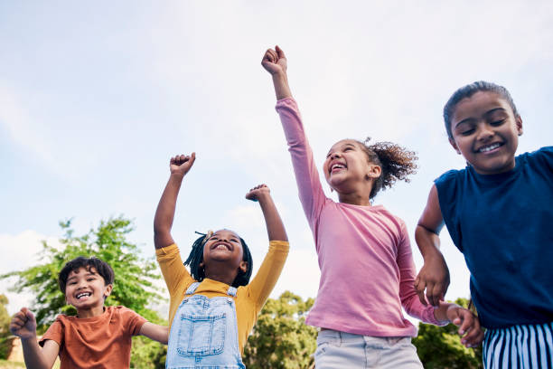 children, freedom and energy with friends cheering together outdoor while having fun during the day. kids, energy or diversity with a girl and boy group playing or bonding outside in summer - elementary student imagens e fotografias de stock