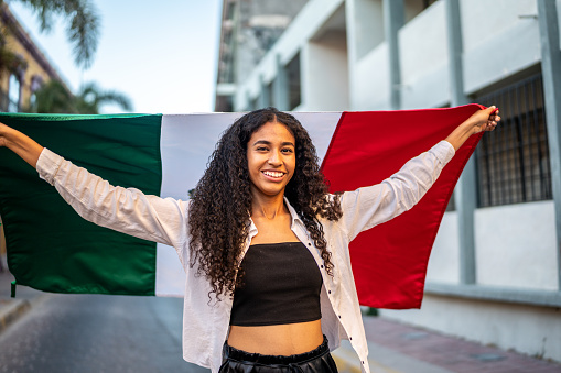 Portrait of young woman holding a mexican flag on the street