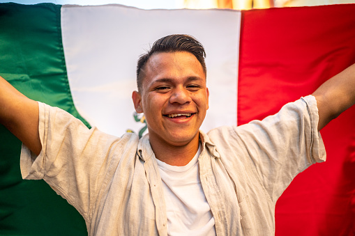 Portrait of a young man walking while holding a mexican flag in the street