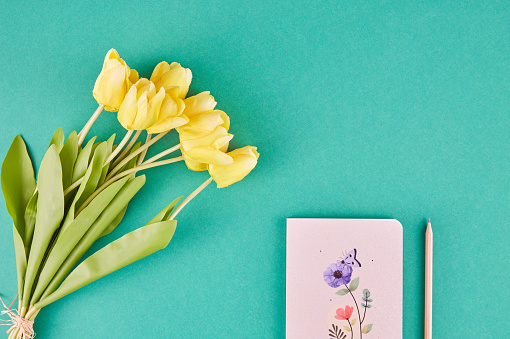 Yellow Tulips, Notebook And Pencil Over Green Background