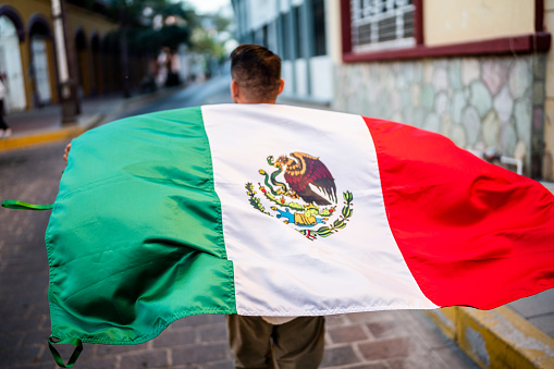 Man walking while holding a mexican flag in the street