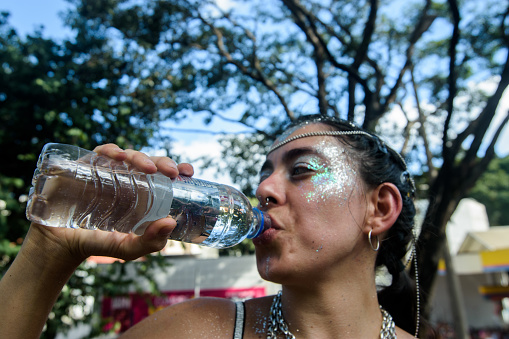 Woman drinking water in a carnival block.\nBelo Horizonte Carnival