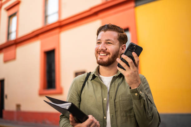 giovane uomo ascolta il messaggio audio usando il telefono cellulare all'aperto - main street audio foto e immagini stock