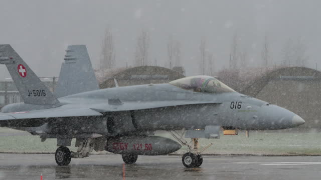 Pair of defence aircraft taxi down the runway for take-off during a snowfall