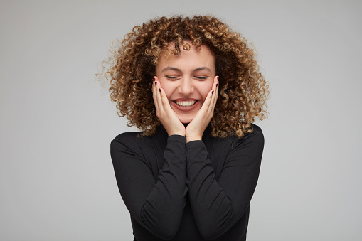 Young woman with curly hair putting hands on cheeks, posing happiness.