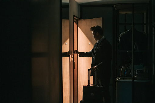 in silhouette Asian Chinese businessman walking into hotel room inserting hotel keycard activate electricity of the room