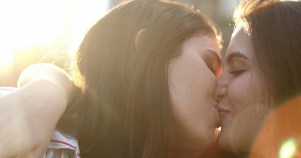 Young women in romantic moment between two gay lesbian girlfriends outside with lens-flare stock photo