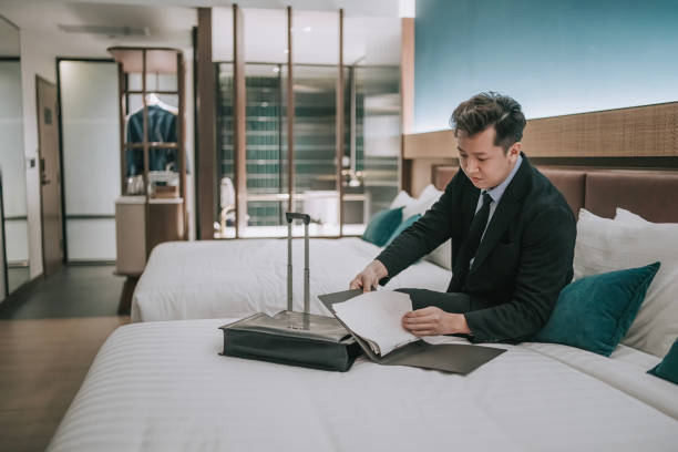 istock Asian businessman working in hotel room sitting on bed reading file documents 1475863137