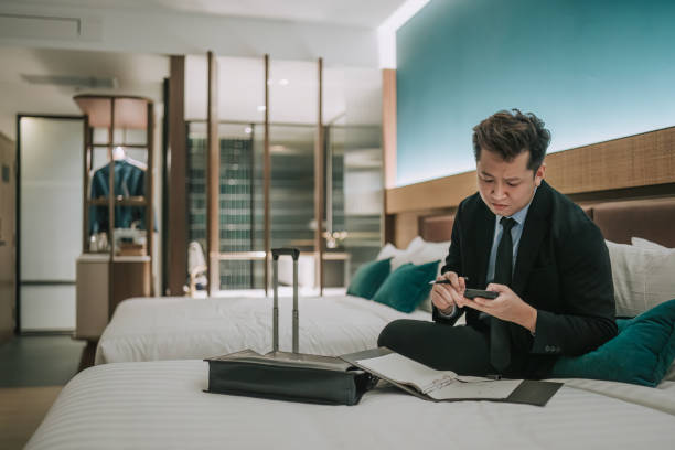 istock Asian businessman working in hotel room sitting on bed writing notes reading phone text messages 1475863238