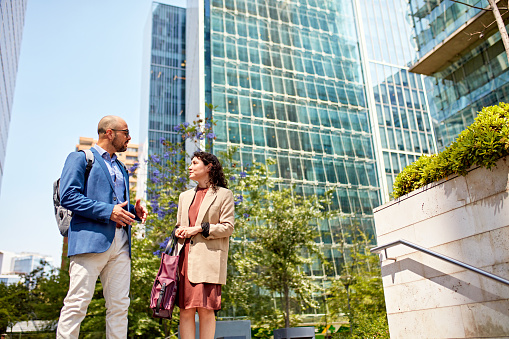 Male and female professionals in their 30s standing face to face in springtime sunshine and interacting.