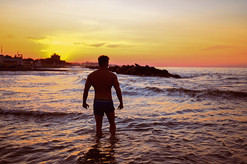 mid adult man standing against a sunset sky in a sea water.