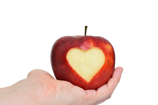 Fresh juicy apple with heart shaped cutout in female hand, isolated on white background