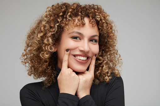 Portrait of smiling curly-haired young woman putting her fingers near her lips.