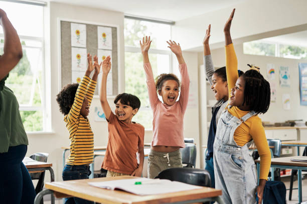 Kids, fun stretching and classroom hands in the air for happy children assessment growth in a school. Students, exercise and happiness of young group in a education study hall with student motivation stock photo