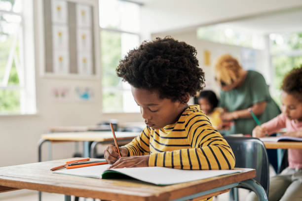 istock Education, writing and learning with child in classroom for knowledge, information and academic development. Study, focus and serious with black boy and students in school for exam concentration 1475870317