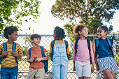 istock Children talking, playground happiness and kids in a park ready for fun with friends in summer. School backpack, morning and diversity of young people together with a smile feeling happy outside 1475870392
