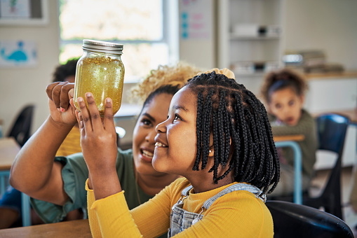 Education, class and teacher with a child with a jar for a scientific experiment, project or research. Discovery, learning and female science educator helping a girl student with assignment at school