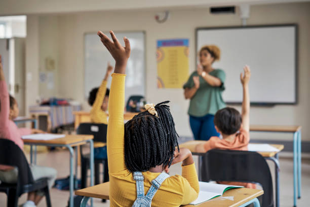 Questions, teacher or education at school with kids hands raised to answer English language assessment. Classroom, learning or tutor teaching summary information to smart and clever group of children stock photo