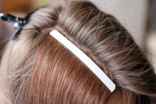 Hair ribbons for extensions on a woman's head at home. Hair extensions to thicken your own. Individual strands of hair close-up
