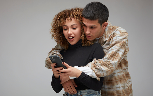 Young curly-haired woman showing her boyfriend something interesting on her phone. Both were surprised by what they saw.