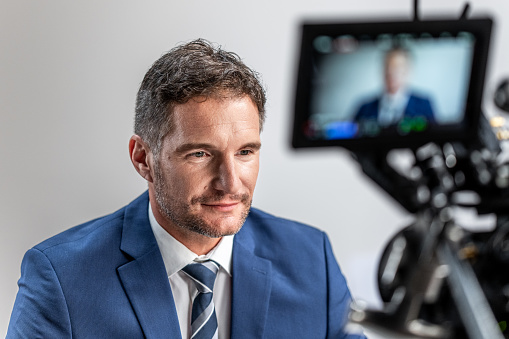 Businessman sitting in front of professional camera in television studio medium shot