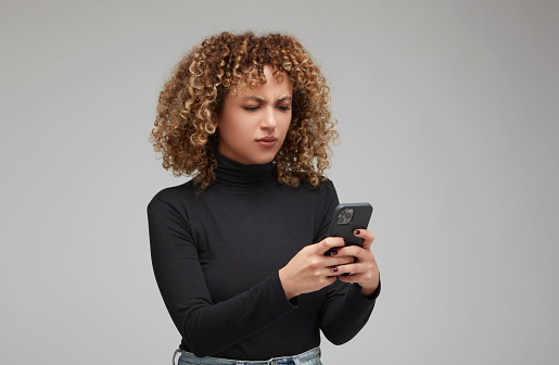 Curly-haired woman looking worriedly at something on her cell phone.