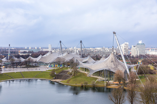 Munich, Germany – March 12, 2023: Olympiahalle at Olympic Park, Olympic village in background, lake in foreground