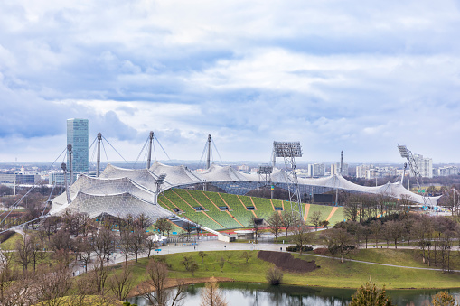 Munich, Germany – March 12, 2023: Olympic Stadium at Olympic Park, Olympic village in background, lake in foreground