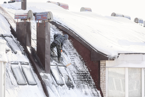 Cherepovets, Russia - February 25, 2023. The climber on the roof cleans windows from ice. Work at height.
